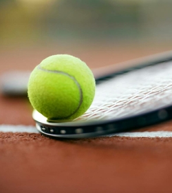 A tennis ball rests on a tennis racket on the clay court.