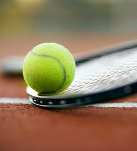 A tennis ball rests on a tennis racket on the clay court.