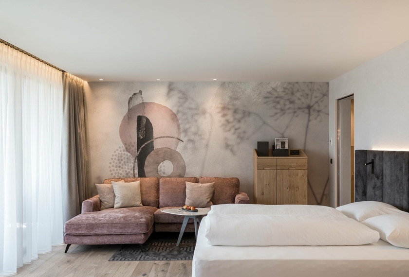 Suite con zona giorno al Feldhof DolceVita Resort Una suite moderna con letto matrimoniale, divano e parete decorativa al Feldhof DolceVita Resort.