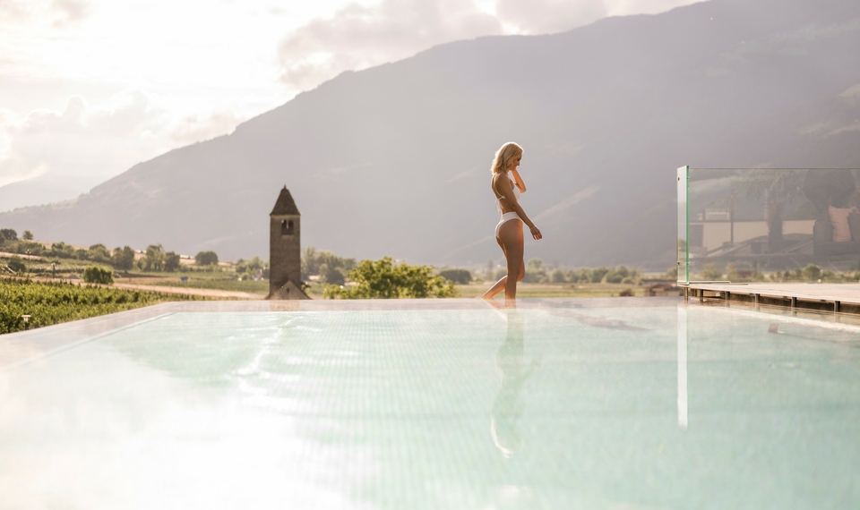 Infinity Pool mit Bergblick im Feldhof Eine Frau steht am Rand des Infinity-Pools mit Blick auf die Berge im warmen Abendlicht.