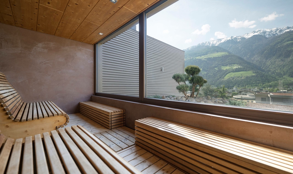 A bright sauna with wooden loungers and a large panoramic window overlooking the mountains.