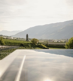 Una sky infinity pool si affaccia sulla valle, sui vigneti, su un campanile e sulle montagne sullo sfondo.