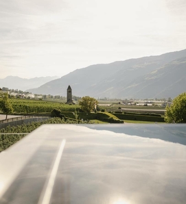 Una sky infinity pool si affaccia sulla valle, sui vigneti, su un campanile e sulle montagne sullo sfondo.