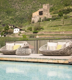 Due poltrone lounge con cuscini sono accanto alla piscina, con paesaggio montano e castello sullo sfondo.