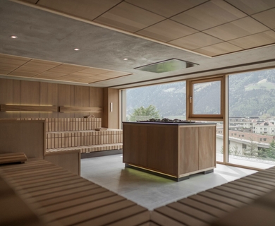 Sauna mit Panoramablick im Feldhof Eine helle Sauna mit Holzsitzbänken, Mittelbank und großen Fenstern mit Blick auf den Ort.