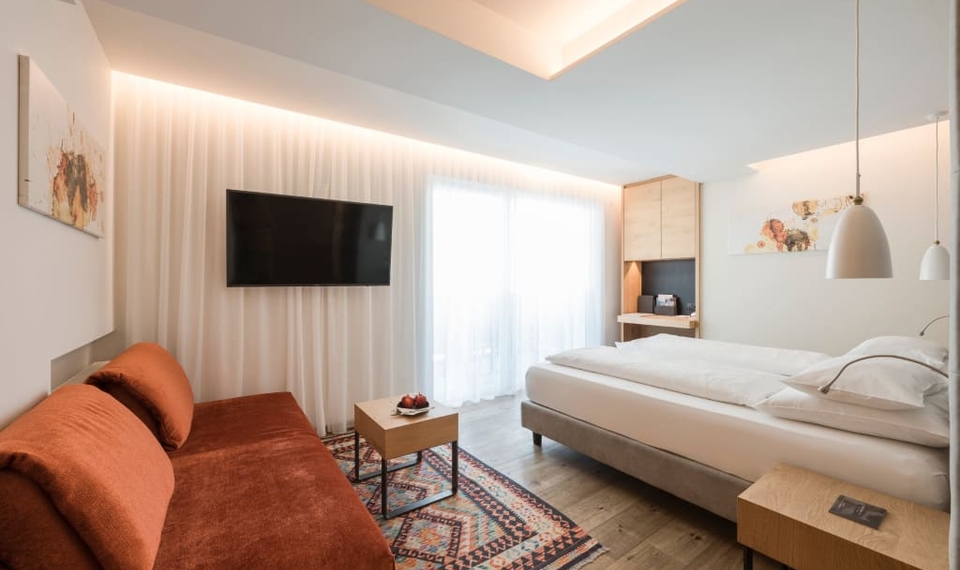 Ein helles Doppelzimmer mit Bett, Sofa, Fernseher und Balkonzugang im Feldhof.