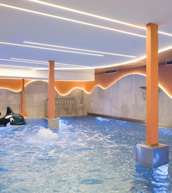 Ein Hallenbad im Family Spa mit Wasserspielen, orangefarbenen Säulen und einem Orca-Spielgerät im Wasser.