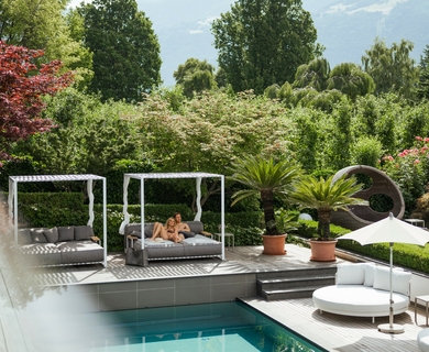 Pool-Lounge im Feldhof DolceVita Resort Eine Pool-Lounge mit Liegen, Sonnenschirm und Pool vor grüner Gartenkulisse.