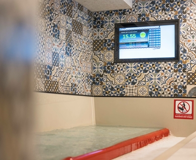 Kinder-Erlebnishallenbad im Family Spa Feldhof Ein Kinder-Erlebnishallenbad mit flachem Wasser, roter Rutsche und Wandbildschirm im Family Spa.