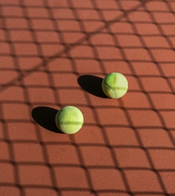 Two tennis balls lie on a tennis court with the shadow of a net across the surface.