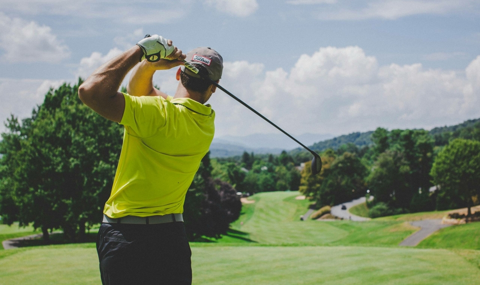 A golfer takes a swing on a well-kept golf course with hills and trees in the background.