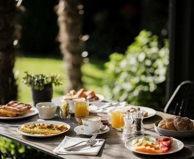 Frühstückstisch im Hotelgarten Ein gedeckter Frühstückstisch mit Gebäck, Obst, Kaffee und Orangensaft steht im Garten.