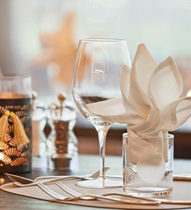 Ein elegant gedeckter Tisch mit Weinglas, Besteck und gefalteter Serviette im Hotelrestaurant.