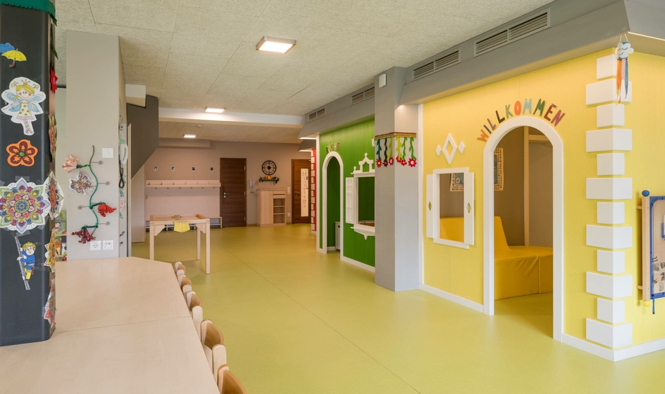 Bunter Betreuungsraum für Kinder mit kleinen Türen, Tischen und einer Bank.
