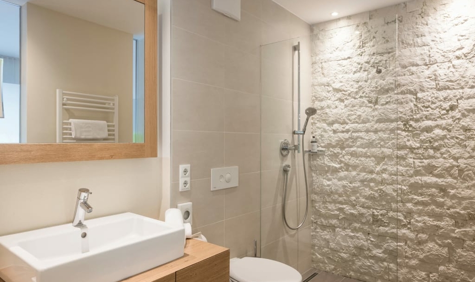 Ein modernes Bad mit Waschbecken, Spiegel und Dusche neben der Toilette.