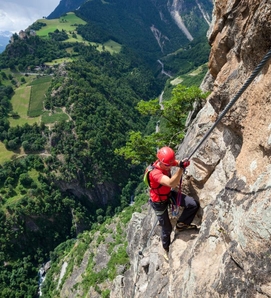 Eine Person klettert gesichert an einer steilen Felswand mit Blick ins grüne Tal in Südtirol.