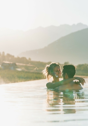 A couple embraces in the infinity pool with mountains in the background and warm evening light.