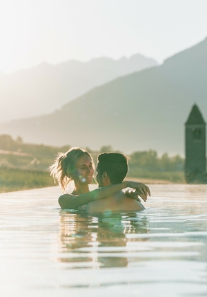 A couple embraces in the infinity pool with mountains in the background and warm evening light.