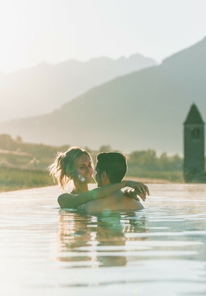 Ein Paar umarmt sich im Infinity-Pool vor der Bergkulisse bei warmem Abendlicht.