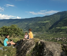 Eine Familie sitzt auf einem Felsen und blickt über das Tal und die Berge bei Naturns.
