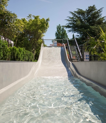 Wasserrutsche im Familienhotel in Naturns Eine Wasserrutsche führt in ein flaches Becken, umgeben von Bäumen und dichtem Grün.