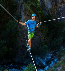 Un uomo assicurato si bilancia su un cavo in un percorso acrobatico davanti a una parete rocciosa.