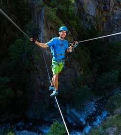Un uomo assicurato si bilancia su un cavo in un percorso acrobatico davanti a una parete rocciosa.