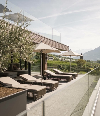 Ruhebereich auf der Sonnenterrasse im Wellnesshotel Liegen und Sonnenschirme auf einer modernen Terrasse mit Blick in die grüne Landschaft.