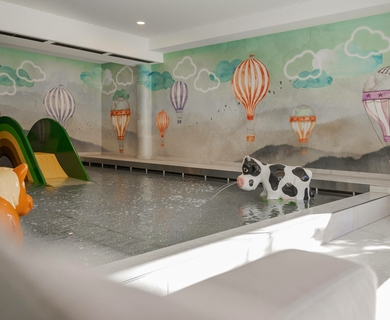 Kinder-Erlebnishallenbad im Family Spa Ein Kinder-Erlebnishallenbad mit Rutsche, Tierfiguren und Luftballon-Malerei an den Wänden.
