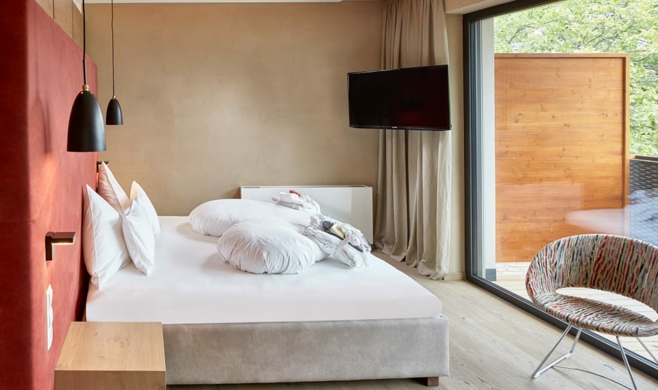 Chalet-Schlafzimmer mit Blick zur Loggia Ein helles Schlafzimmer im Chalet mit Doppelbett, TV und Blick auf die Loggia durch die große Glasfront.