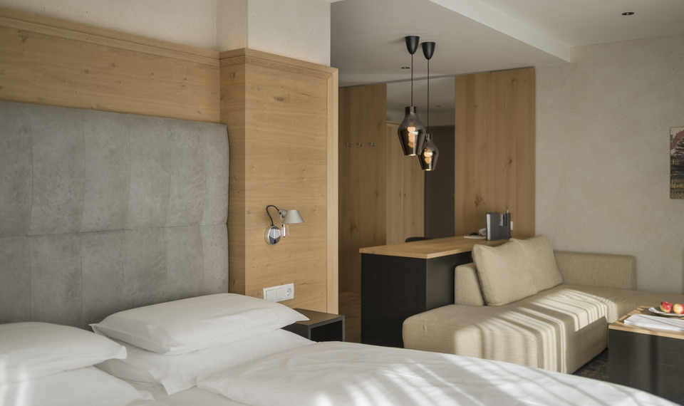 Suite mit Balkon im Feldhof DolceVita Resort Ein modernes Hotelzimmer mit Doppelbett, Sofa und Holzdetails, passend zur Suite Bergzauber mit Balkon.