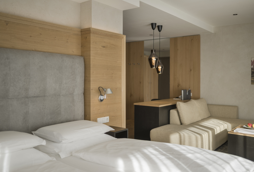 Suite mit Balkon im Feldhof DolceVita Resort Ein modernes Hotelzimmer mit Doppelbett, Sofa und Holzdetails, passend zur Suite Bergzauber mit Balkon.