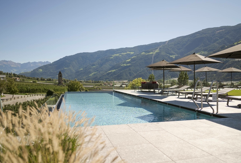 Terrazza piscina con vista monti al Feldhof Naturns Una piscina all’aperto con lettini e ombrelloni si affaccia sulle montagne intorno a Naturno.