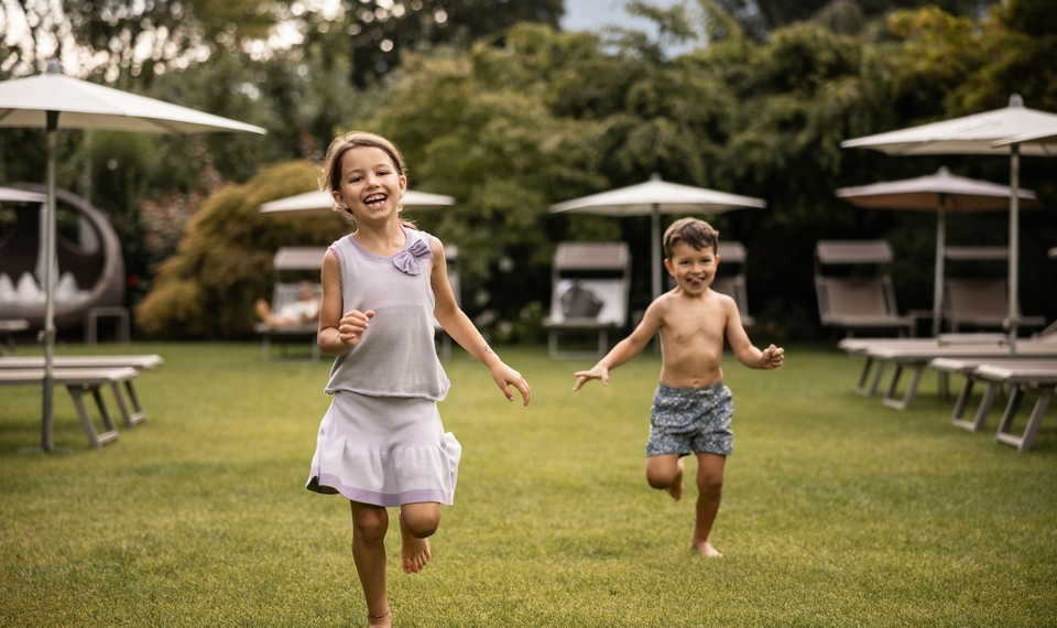 Familienurlaub im Hotelgarten in Naturns Zwei Kinder laufen barfuß über den Rasen im Hotelgarten zwischen Liegen und Sonnenschirmen.