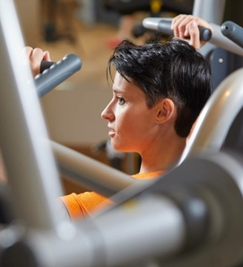Eine Frau trainiert an einer Krafttrainingsmaschine im Fitnessraum.