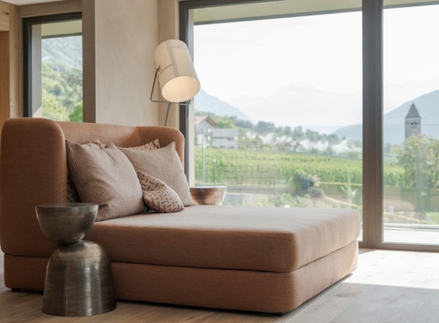 Suite with panoramic view in Naturns A modern lounge with a daybed and large window overlooking the landscape.
