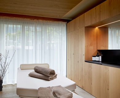 Wellnessliege im Feldhof DolceVita Resort Eine gepolsterte Wellnessliege mit Handtüchern steht vor bodentiefen Vorhängen im hellen Ruheraum.