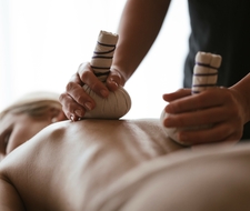 Zwei Hände mit Massagekissen arbeiten am Rücken bei einer Wellnessmassage.