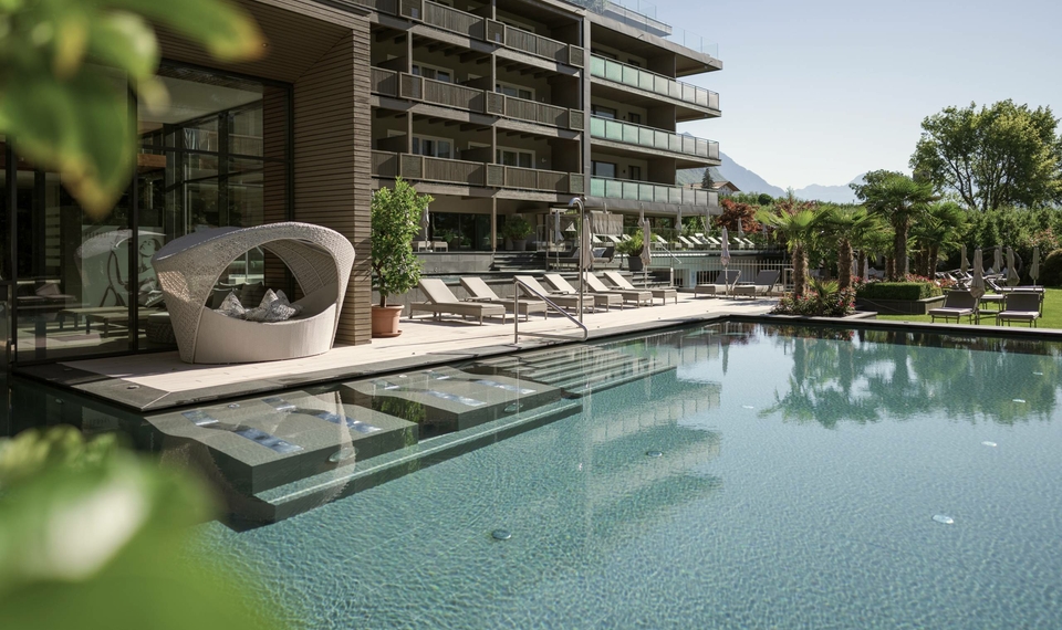 Una piscina esterna con lettini e l'edificio moderno dell'hotel sullo sfondo.