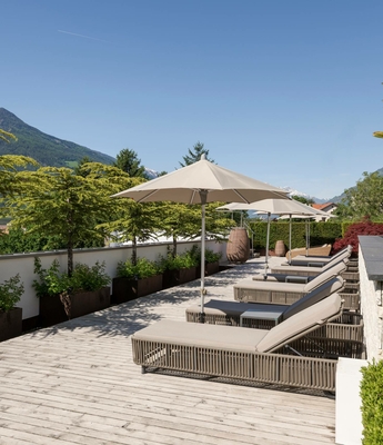 Ruheliegen auf der Sonnenterrasse im Wellnesshotel Sonnenterrasse mit mehreren Ruheliegen, Sonnenschirmen und Blick auf die Berge.
