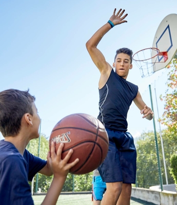 Basketball auf dem Outdoor-Sportplatz Zwei Jugendliche spielen Basketball auf einem Außenplatz mit Korb und blauem Himmel im Hintergrund.