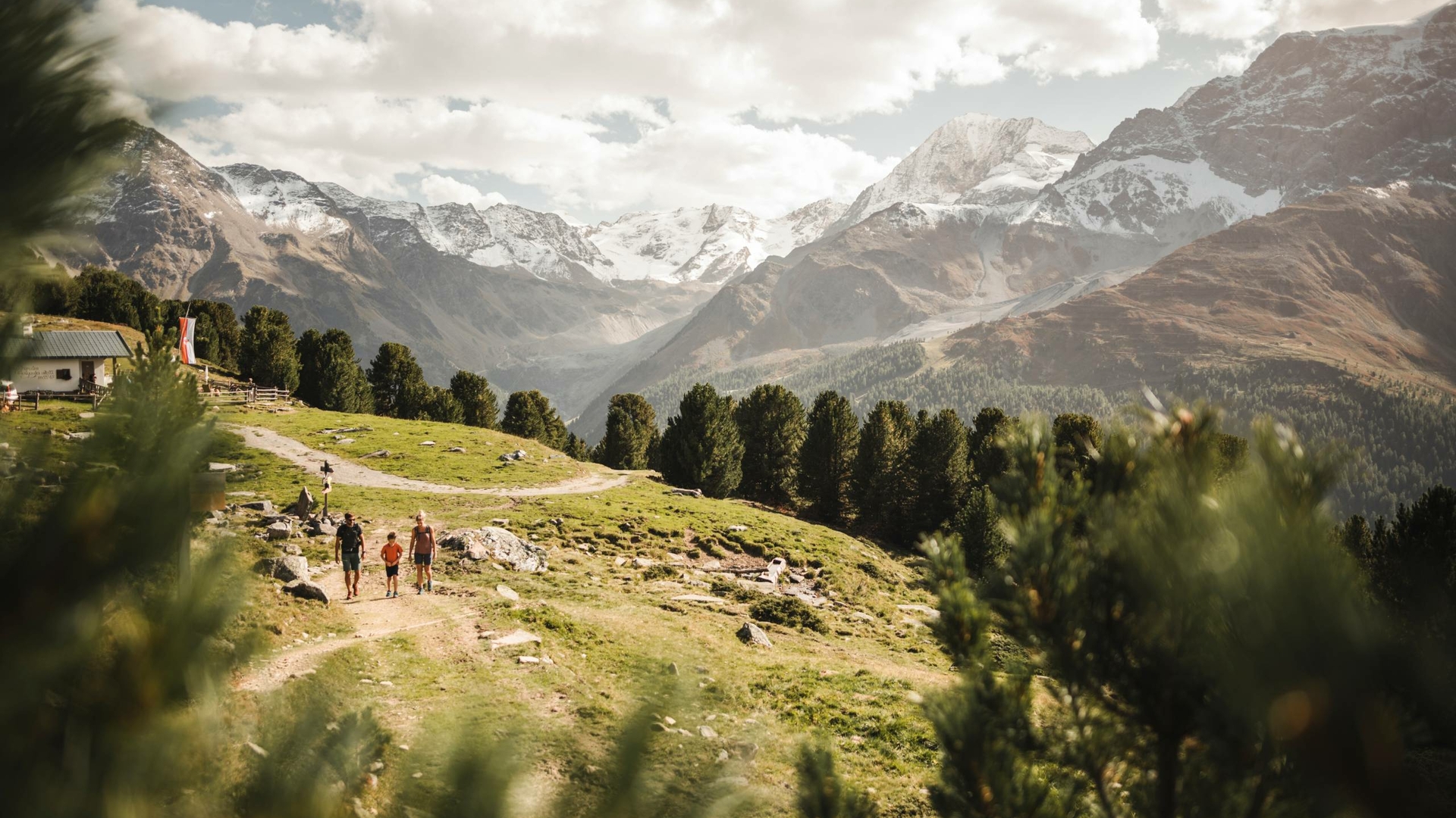 Wanderer gehen über einen Almpfad mit weitem Blick auf die Berge im Meraner Land.