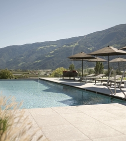 La piscina infinity si trova davanti alle montagne, con lettini e ombrelloni sulla terrazza.