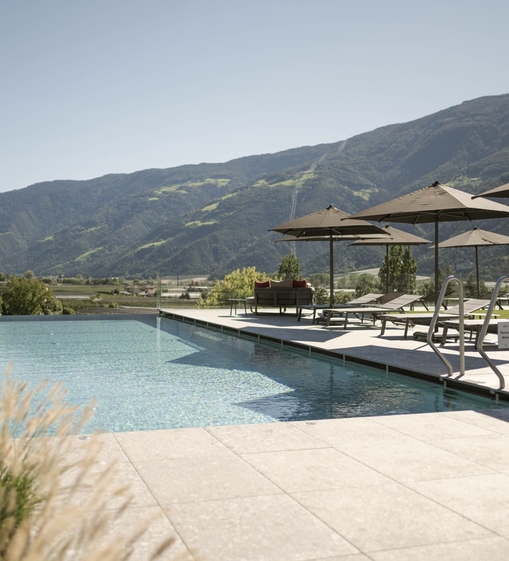 La piscina infinity si trova davanti alle montagne, con lettini e ombrelloni sulla terrazza.