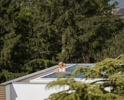 A woman relaxes in the rooftop pool of the Sky Spa, framed by trees and the hotel roofline.