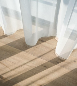 Helle, transparente Vorhänge werfen weiche Schatten auf einen Holzfußboden.