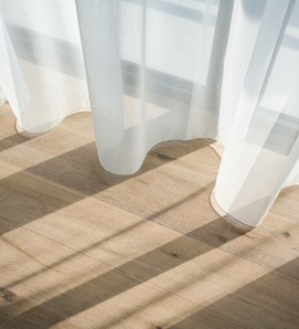 Helle, transparente Vorhänge werfen weiche Schatten auf einen Holzfußboden.