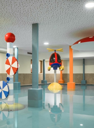 Ein heller Indoor-Kinderpool mit bunten Spielelementen und flachem Wasserbereich.