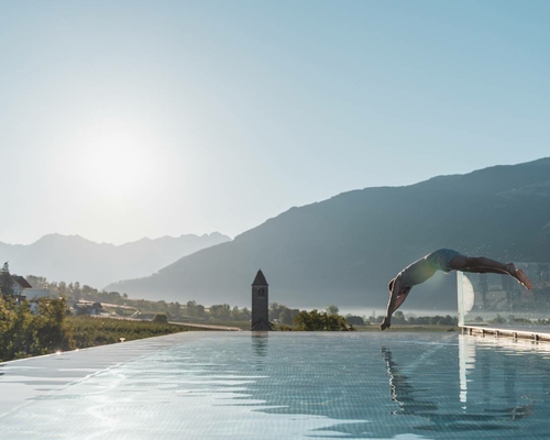 A man dives into the infinity pool with mountains in the background and soft morning light.
