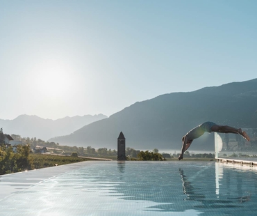 A man dives into the infinity pool with mountains in the background and soft morning light.